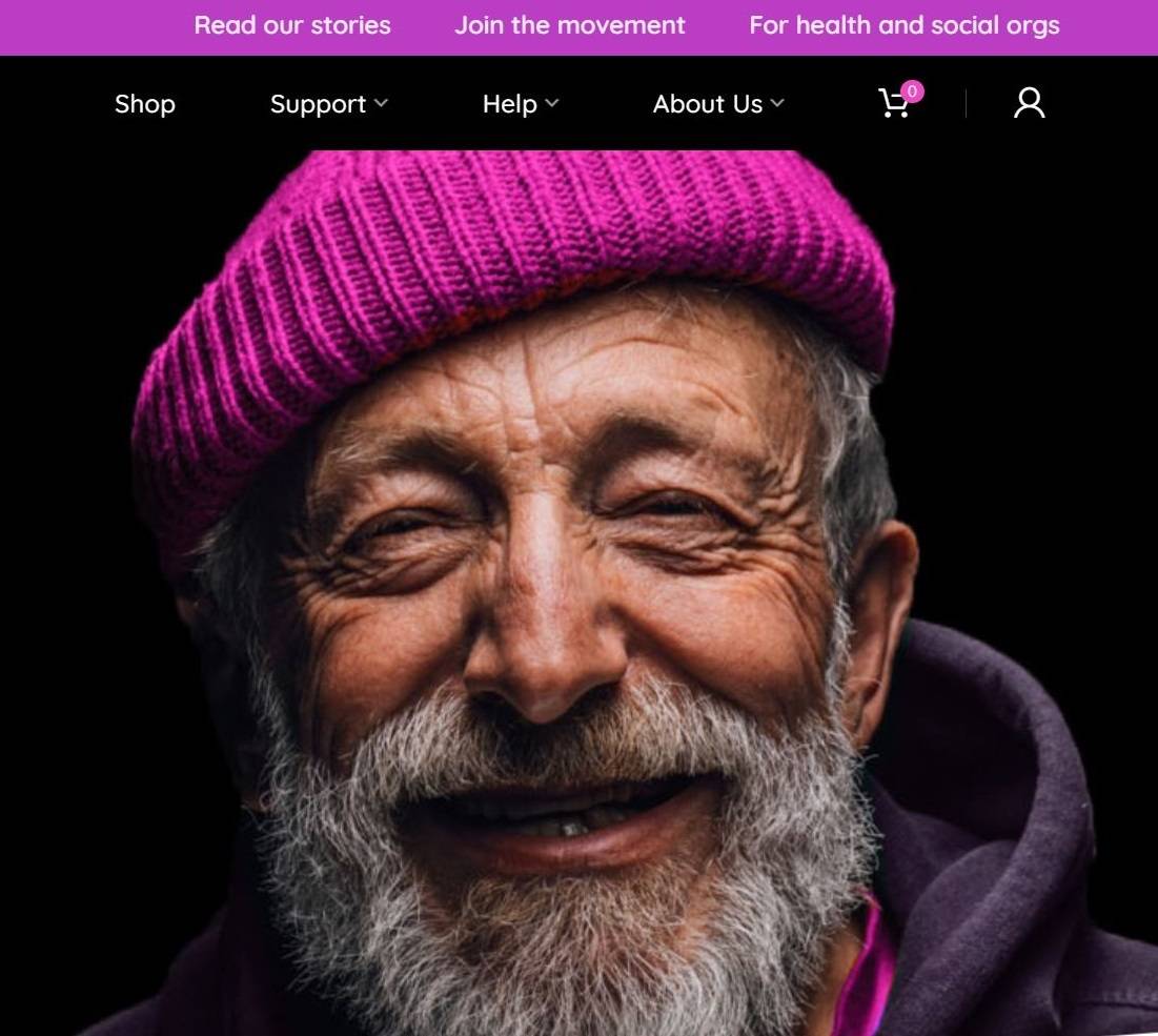 A close-up headshot of a smiling man with a white beard and a magenta-pink beanie fills the frame. The top of the image features a website's navigation bar, partially obscured, with links related to stories and community engagement.